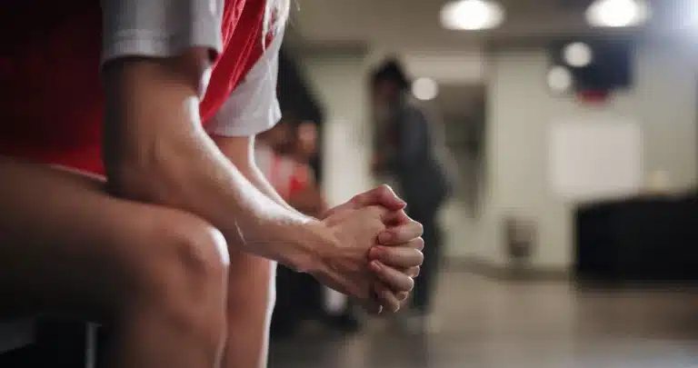 Athlete sitting on the bench with hands clasped, working through pre-competition anxiety